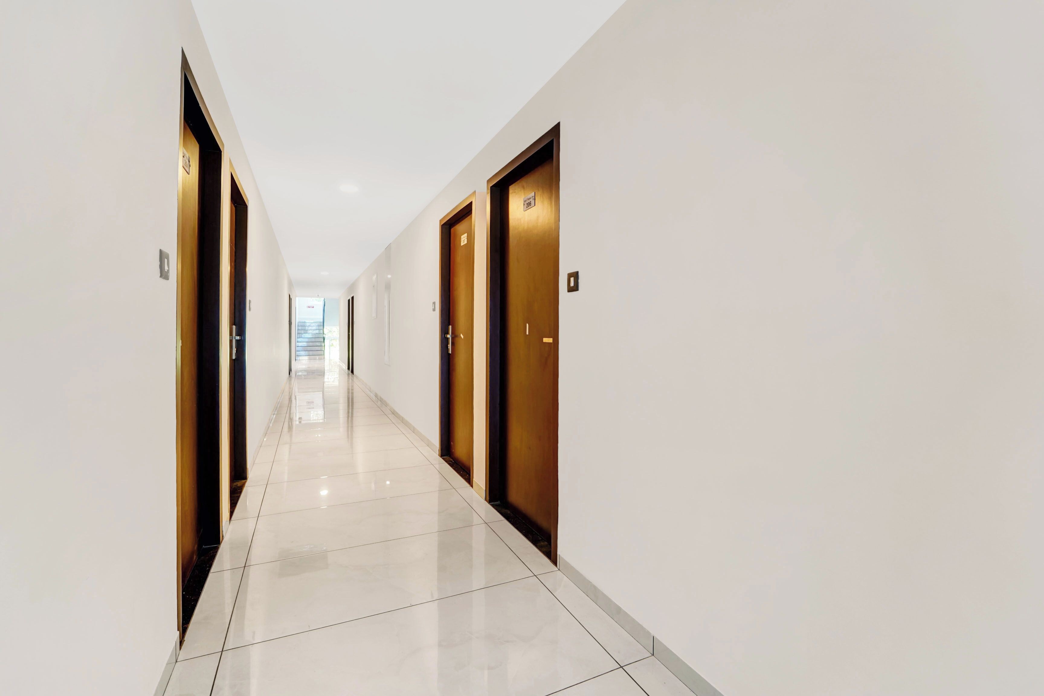 Un pasillo con puertas a ambos lados, que conduce a una habitación luminosa al final.