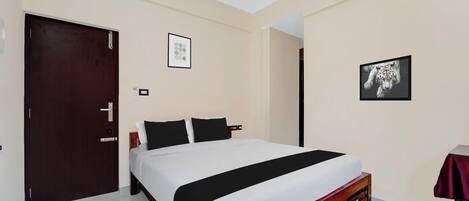 A hotel room with a bed, a door, an air conditioning unit, and two framed pictures on the wall.