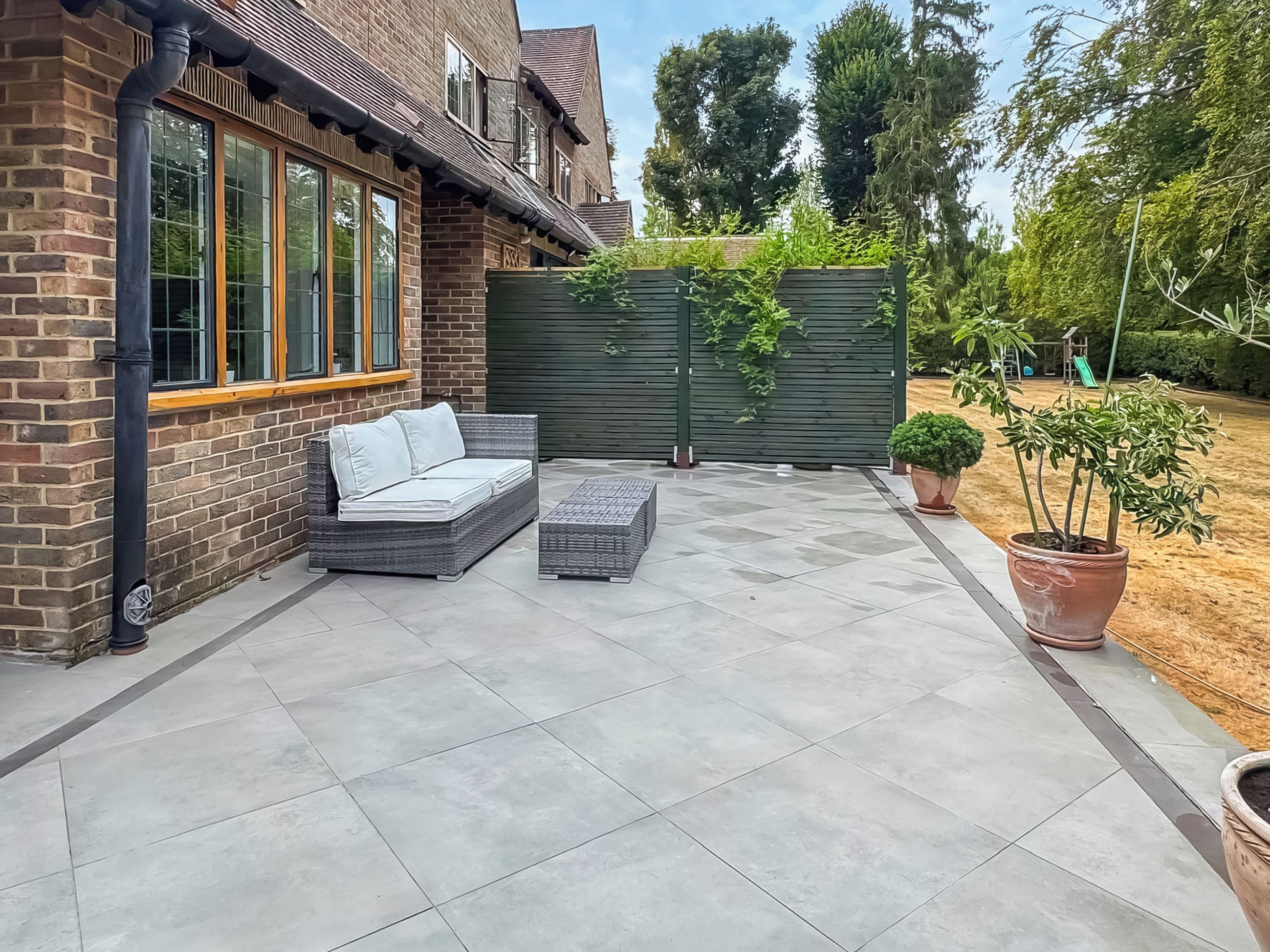 A patio with a sofa and a small table, a brick wall, and a green fence.