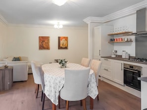 Une cuisine moderne avec des meubles blancs, une table à manger avec des chaises et un canapé dans l’espace salon.