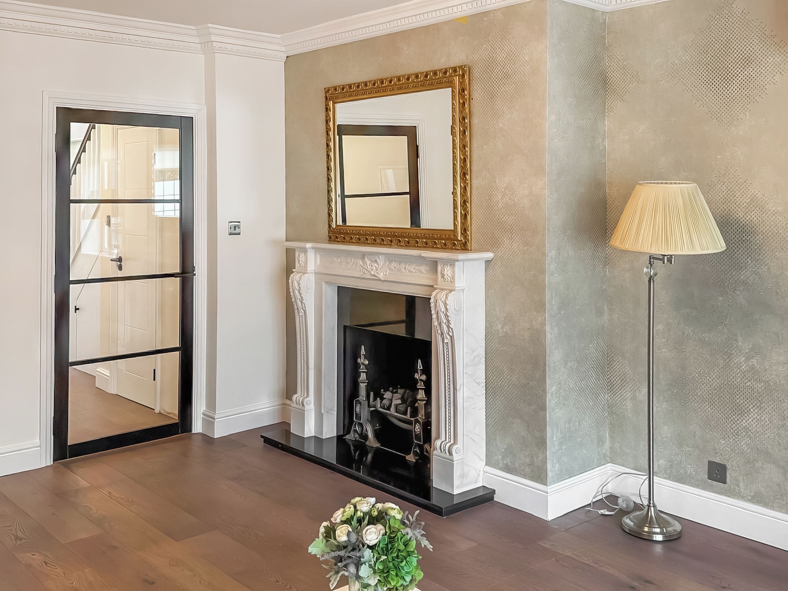 A room with a fireplace, a mirror, a floor lamp, and a door leading to another room.