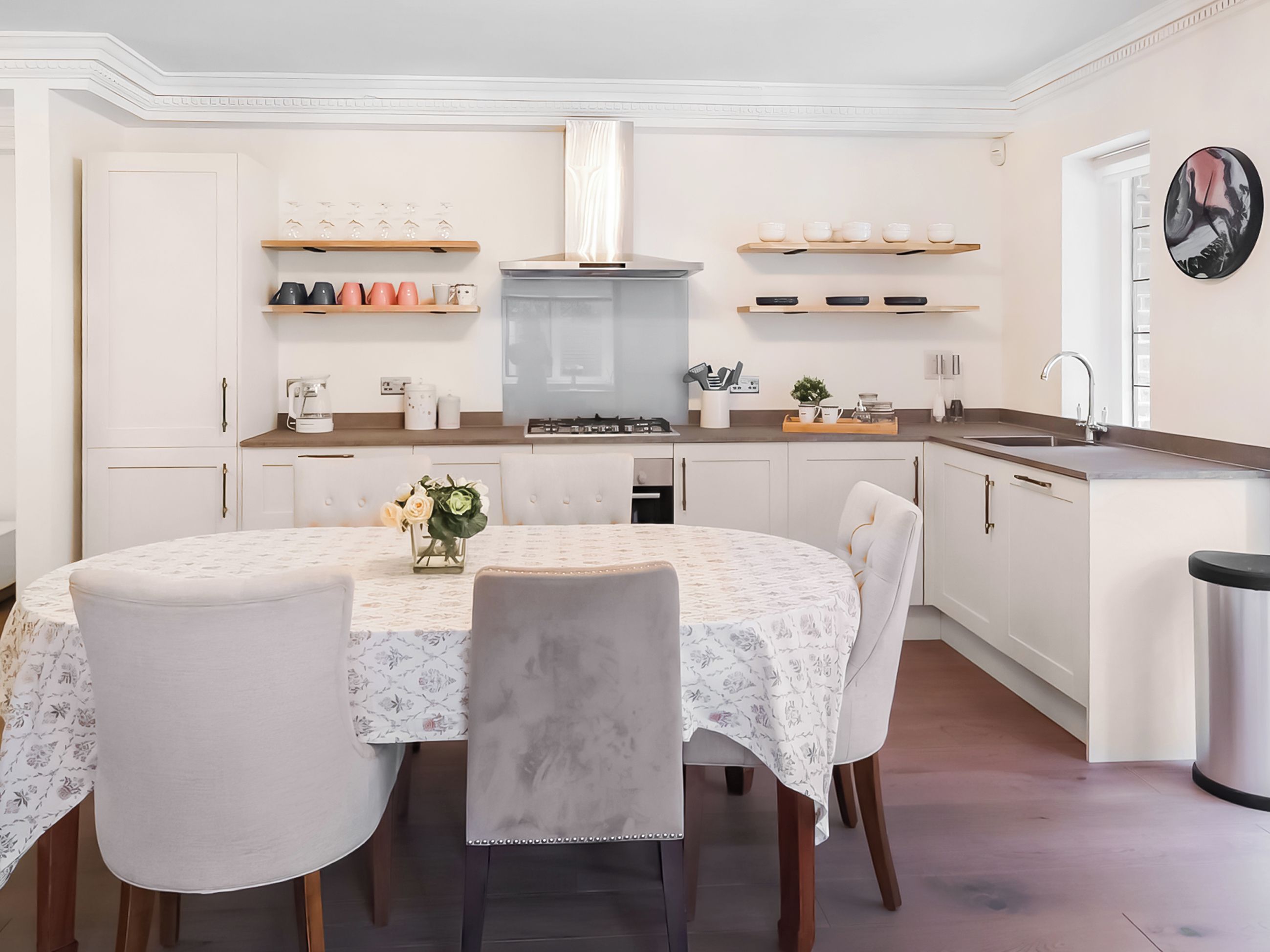 Une cuisine moderne avec des meubles blancs, un îlot central et un coin repas comprenant une table ronde et des chaises.