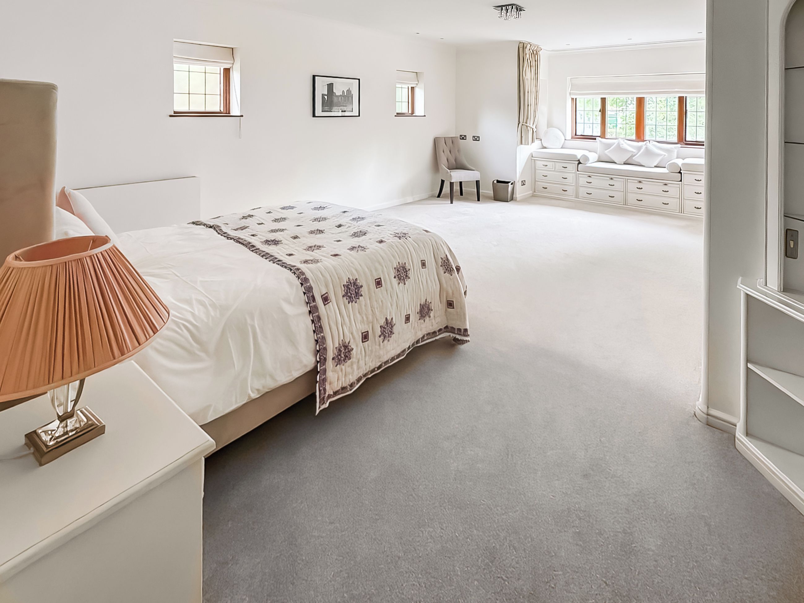 Une chambre spacieuse avec un grand lit, une lampe de chevet, une chaise et une commode.