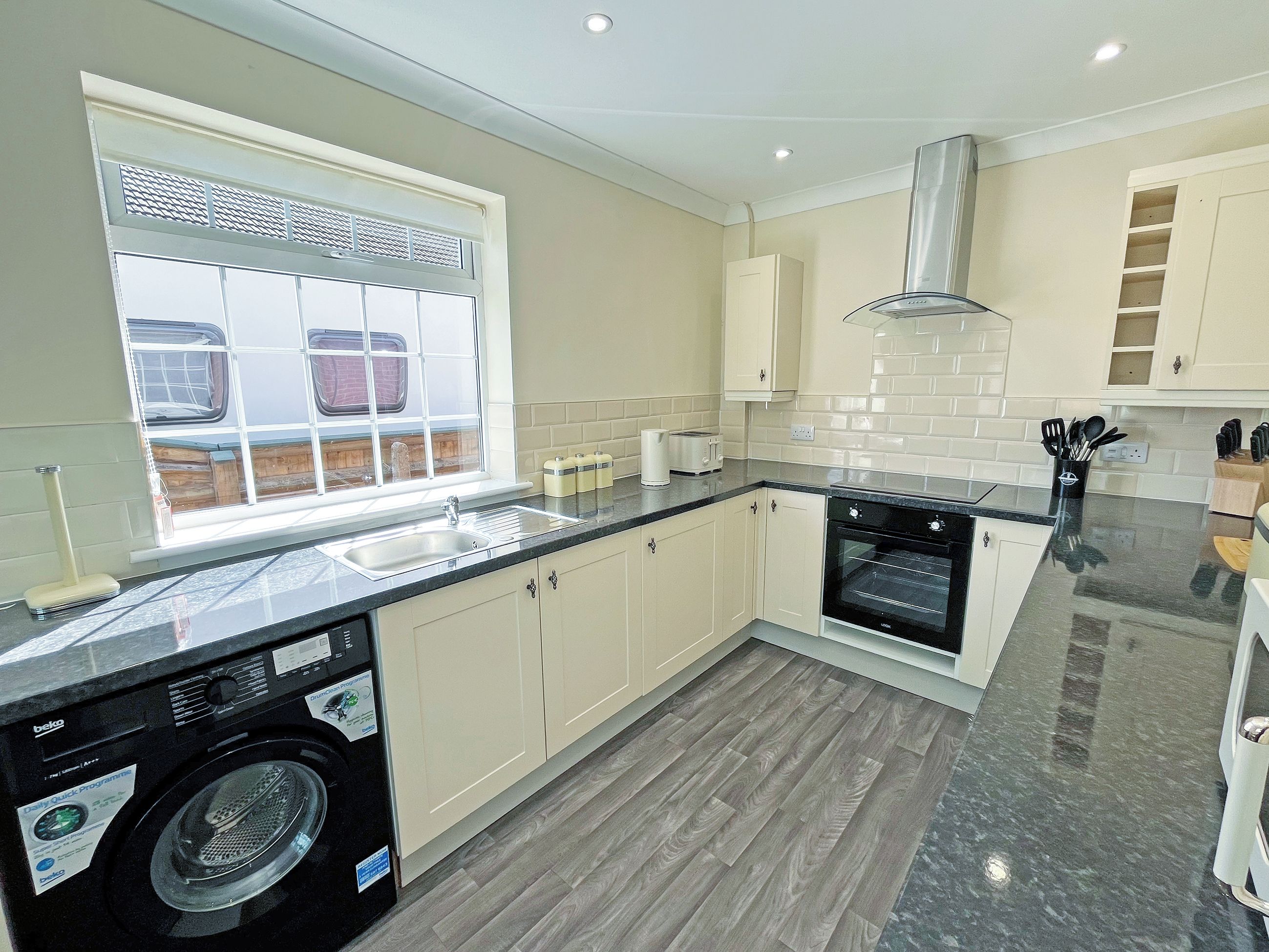 A modern kitchen with a built-in washing machine, a large window, and a stainless steel range hood.