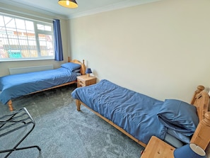 A room with two single beds, a small bedside table with a lamp, a chair, and a window with curtains. - 3 bedroom accommodation in Hogsthorpe (Hogsthorpe)