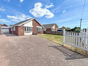A residential property with a paved driveway, a white picket fence, and a brick house with a garage. - 3 bedroom accommodation in Hogsthorpe (Hogsthorpe)