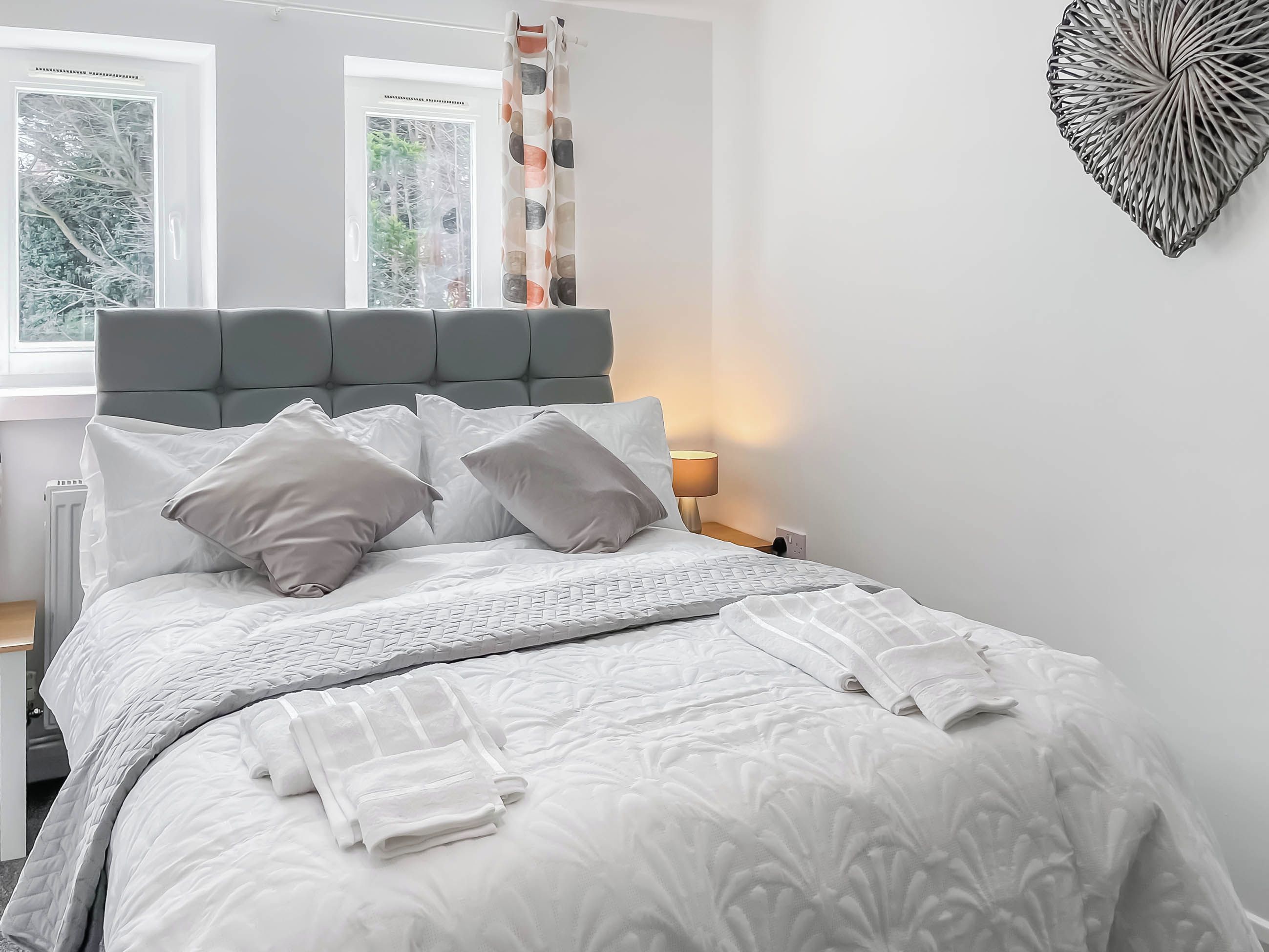 A neatly made bed with a grey headboard, white bedding, and a decorative wall piece.