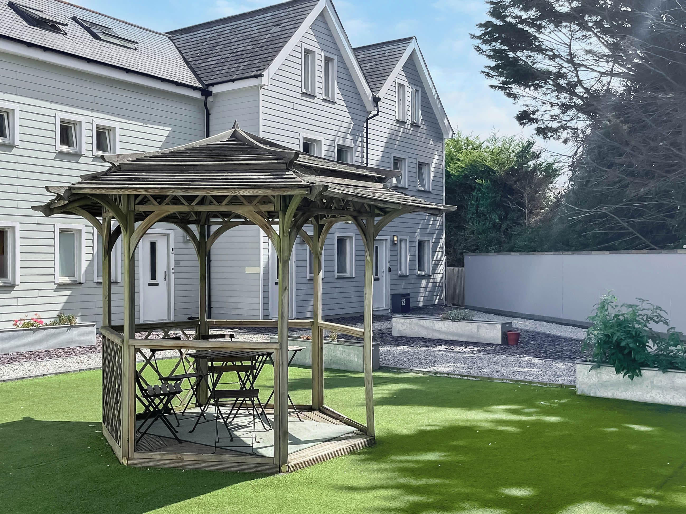 A gazebo with a table and chairs, surrounded by a well-maintained lawn and a house in the background.