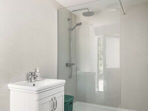 A modern bathroom with a glass-enclosed shower, a white sink, and a green trash bin. - 1 bedroom accommodation in Dorset (Dorset)