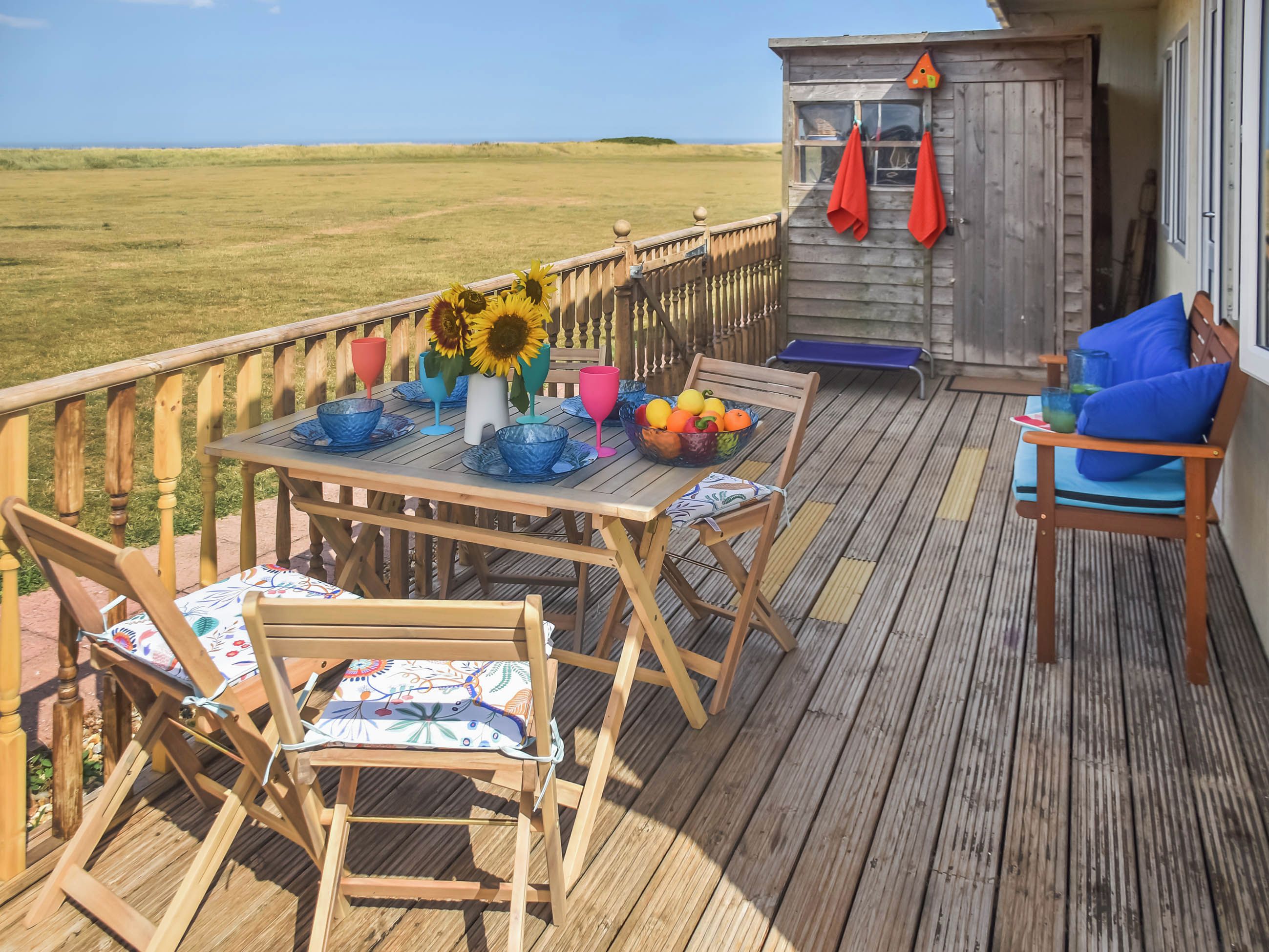 A wooden deck with a table set for dining, chairs, and a small seating area with cushions.