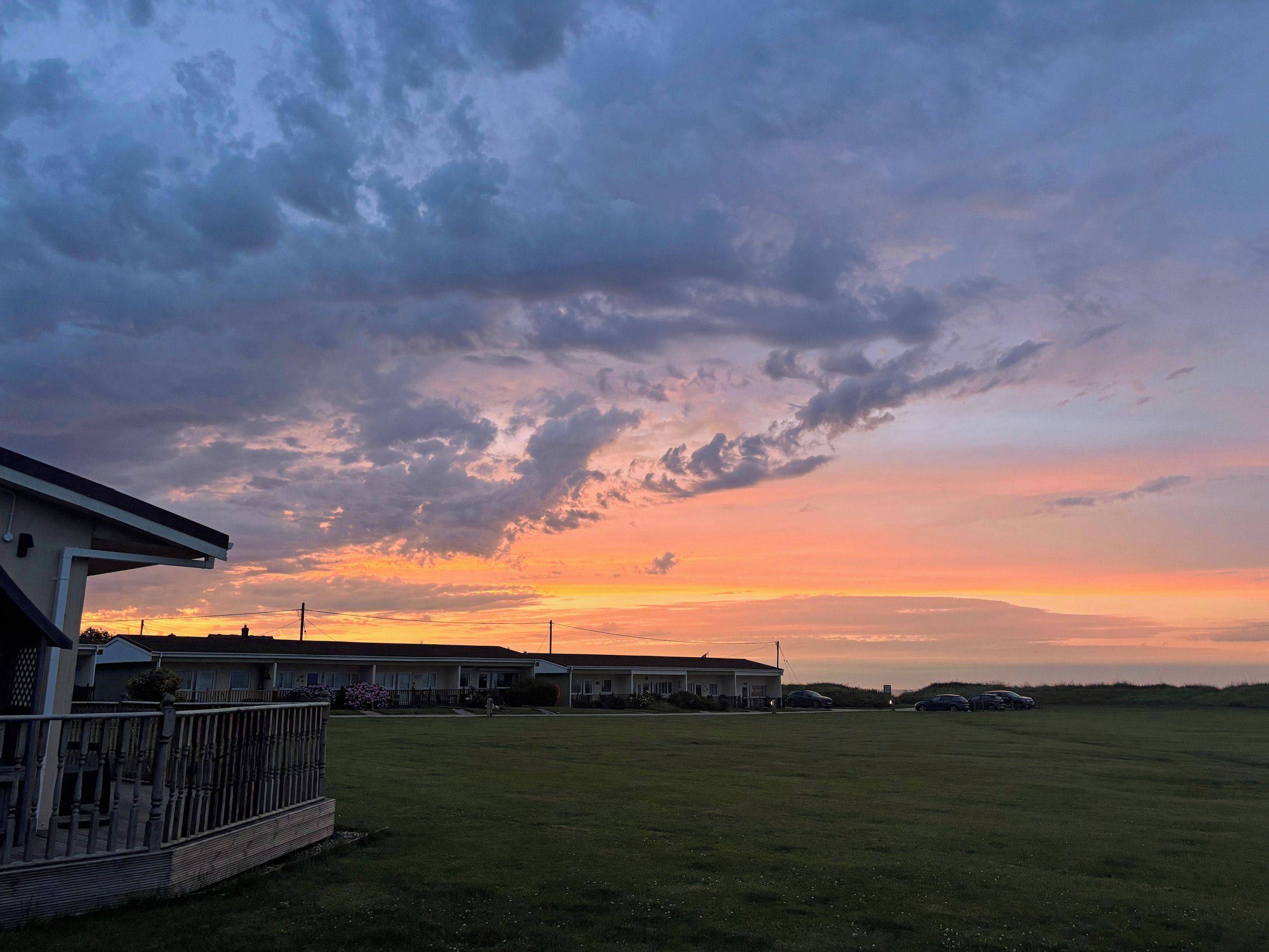 A residential area with houses, a grassy field, and a sunset sky.