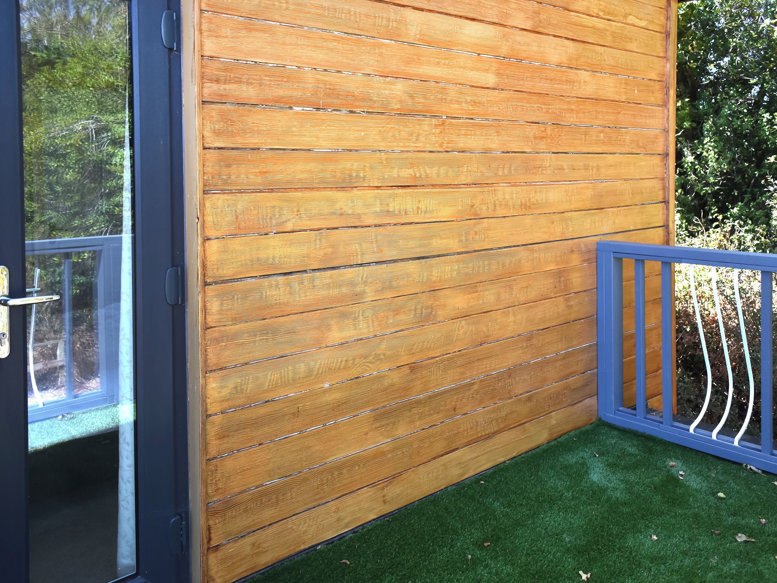 A wooden wall with horizontal planks, a glass door, and a blue metal railing.