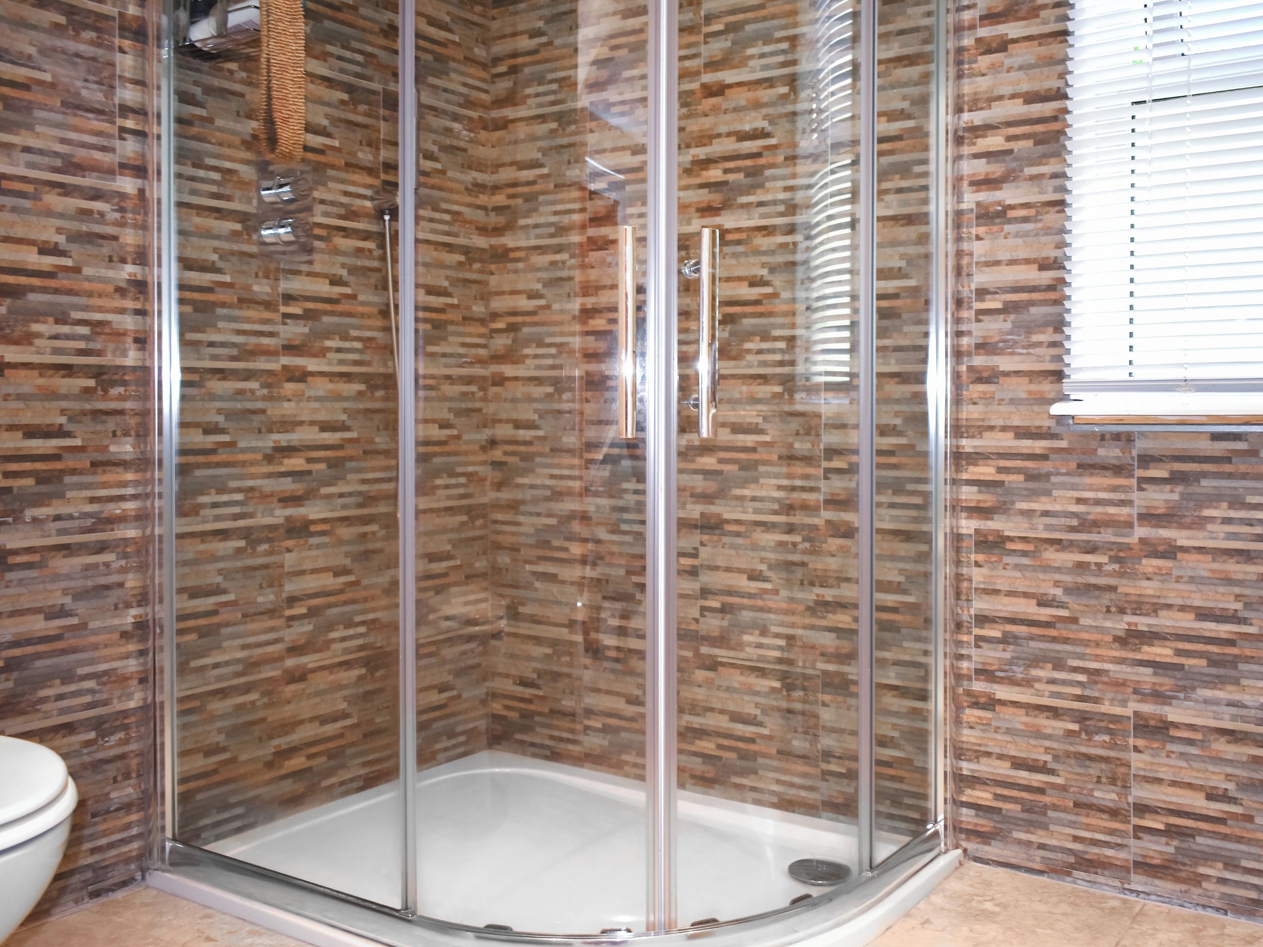 A glass-enclosed shower stall with a tiled wall.