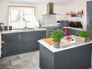 A modern kitchen with a central island, built-in appliances, and a window with blinds. - Crosspark Bungalow Stables (Ashburton)