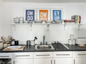 A kitchen with white cabinets, a black countertop, a stainless steel sink, and a coffee machine. There are three framed signs on the wall, and a bookshelf with cookbooks. - 1 bedroom accommodation in Bridlington (Bridlington)