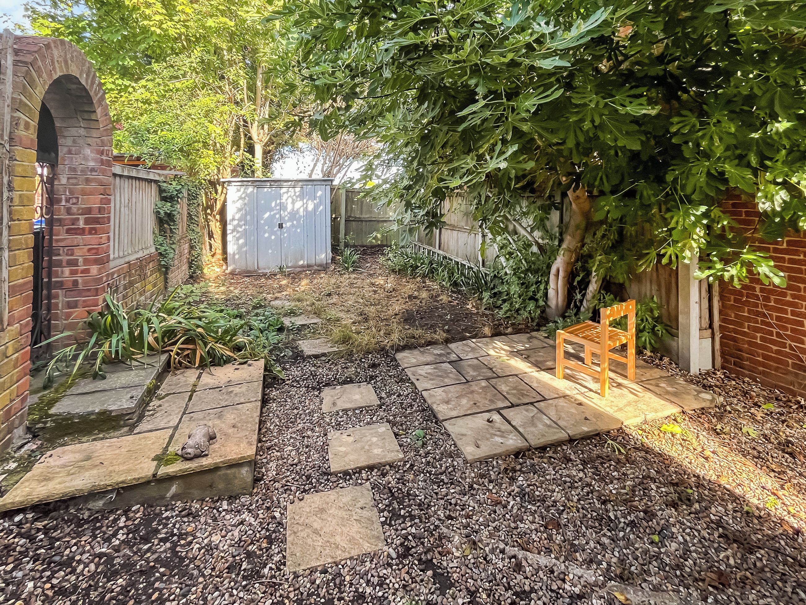 Ein Garten mit einer Backsteinmauer, einer hölzernen Bank und einem Kiesweg.