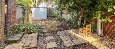 Un jardín con un muro de ladrillo, un banco de madera y un sendero.