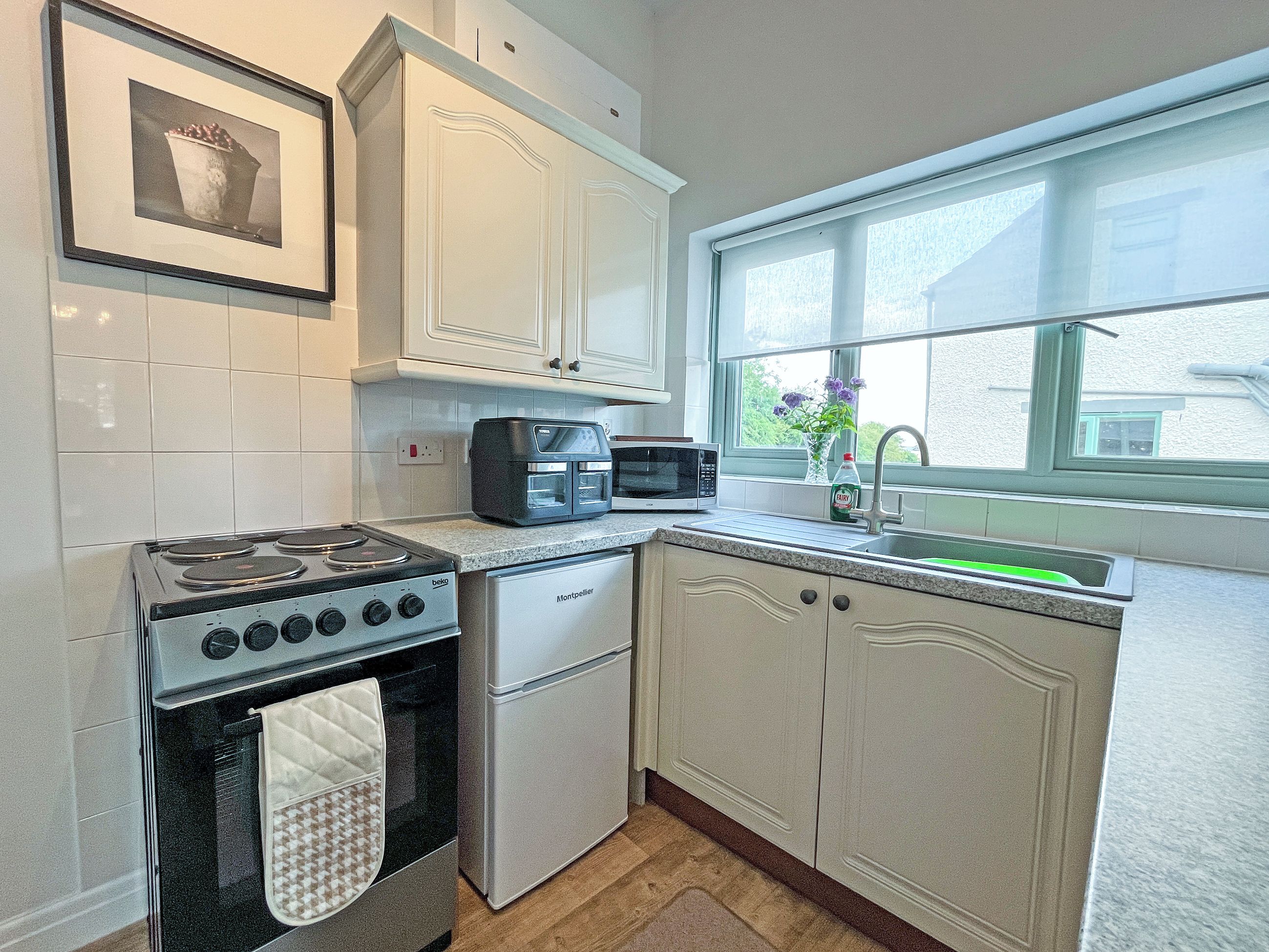 A kitchen with white cabinets, a stove, a microwave, and a sink.