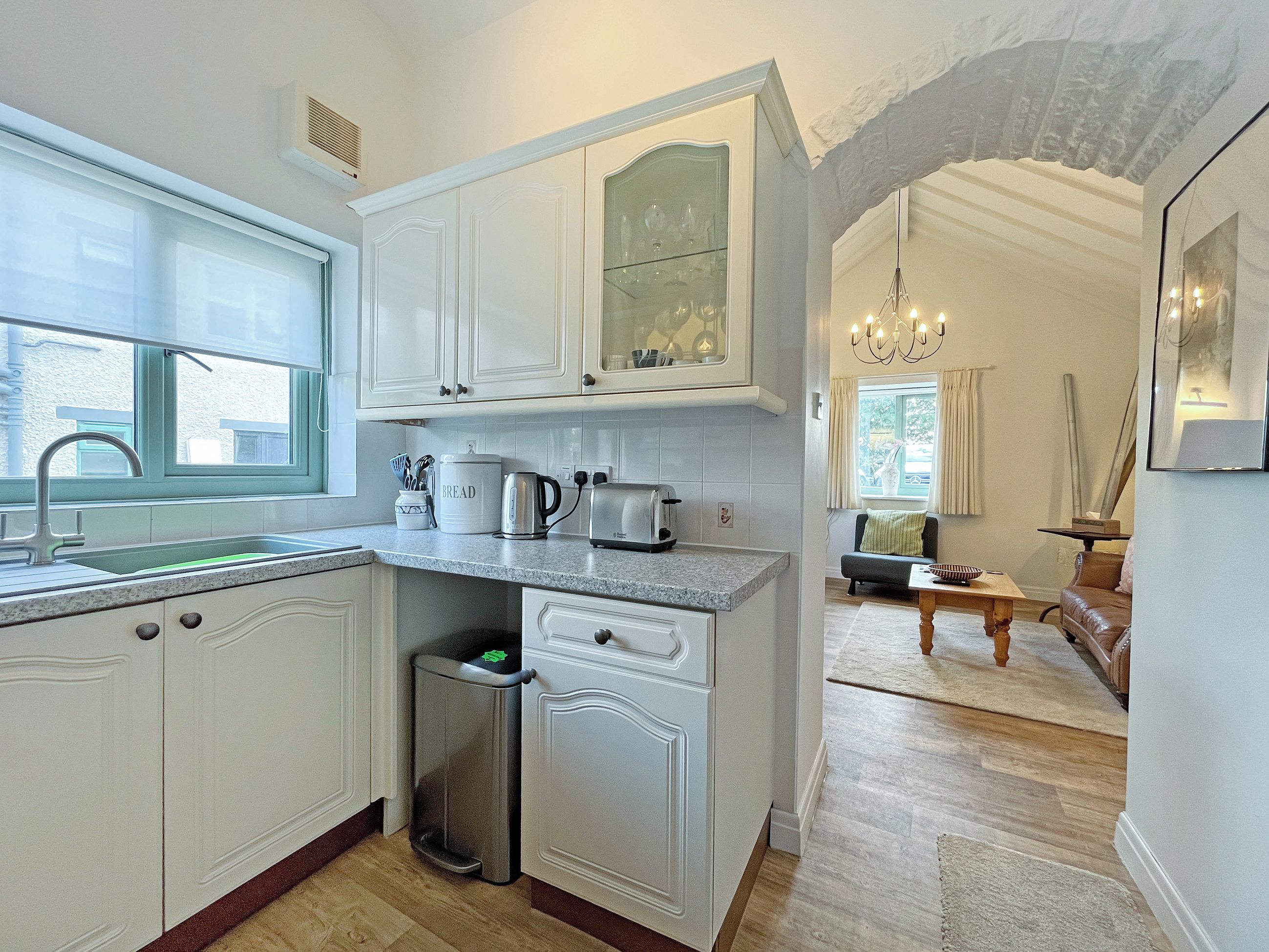 A kitchen with white cabinetry, a sink, a trash bin, and a countertop with a kettle and toaster.