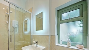 Un baño con ducha acristalada, lavamanos pedestal, inodoro y ventana con vidrio esmerilado.