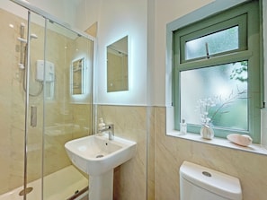 A bathroom with a glass-enclosed shower, a pedestal sink, a toilet, and a window with frosted glass.