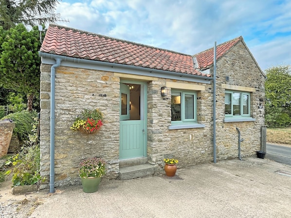 A stone building with a tiled roof, a green door, and potted plants.