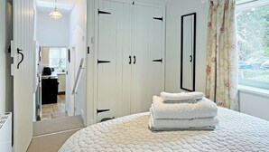 Un dormitorio con cama, armario, espejo y ventana con cortinas.