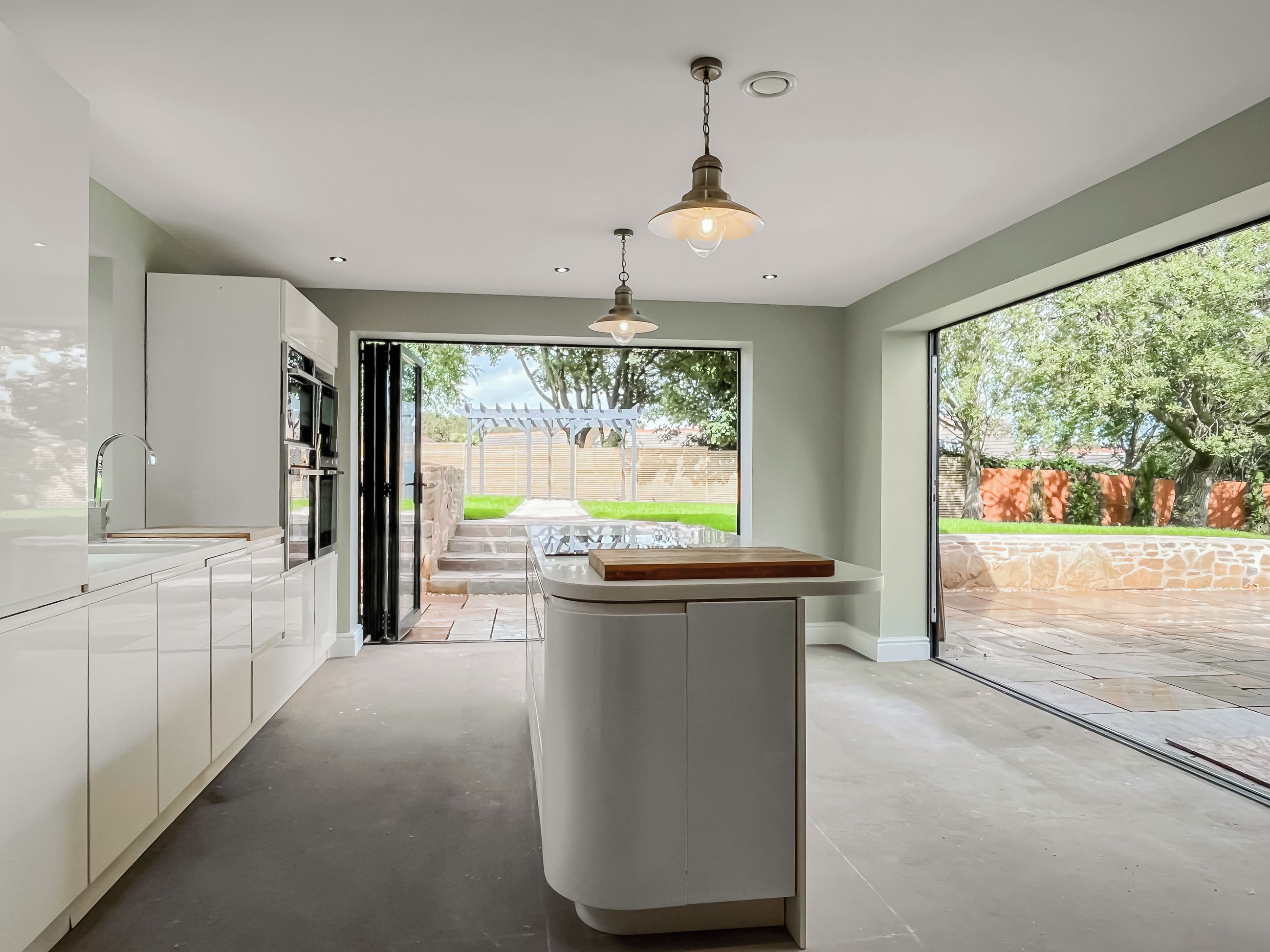 Een moderne keuken met een centraal eiland, een inbouwoven en een groot raam met uitzicht op een tuin.