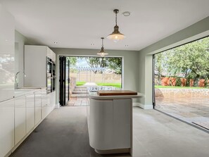 A modern kitchen with a central island, a built-in oven, and a large window overlooking a garden. - Lower Tower Hill Farm (Up Holland, West Lancashire)