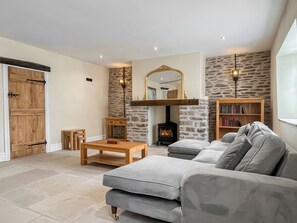 A cozy living room with a stone fireplace, a sofa, a coffee table, and a bookshelf. - Lower Tower Hill Farm (Up Holland, West Lancashire)
