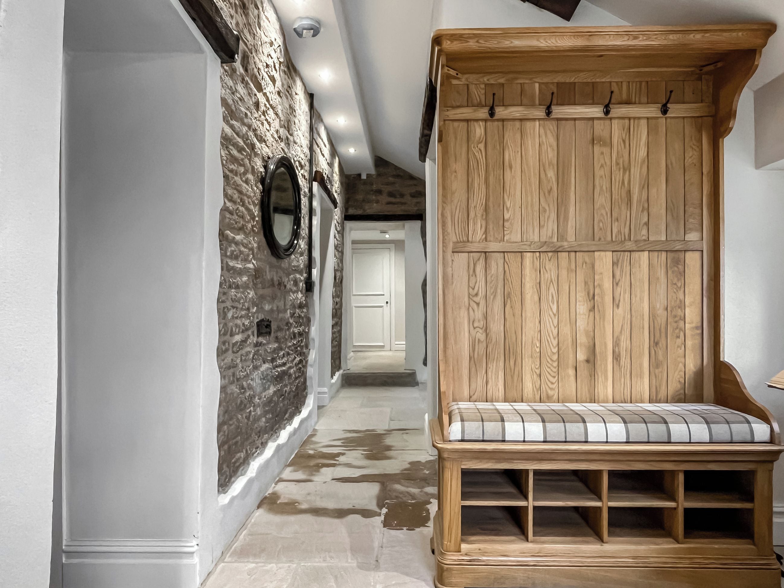 A hallway with a stone wall, wooden bench, and a wooden coat rack.