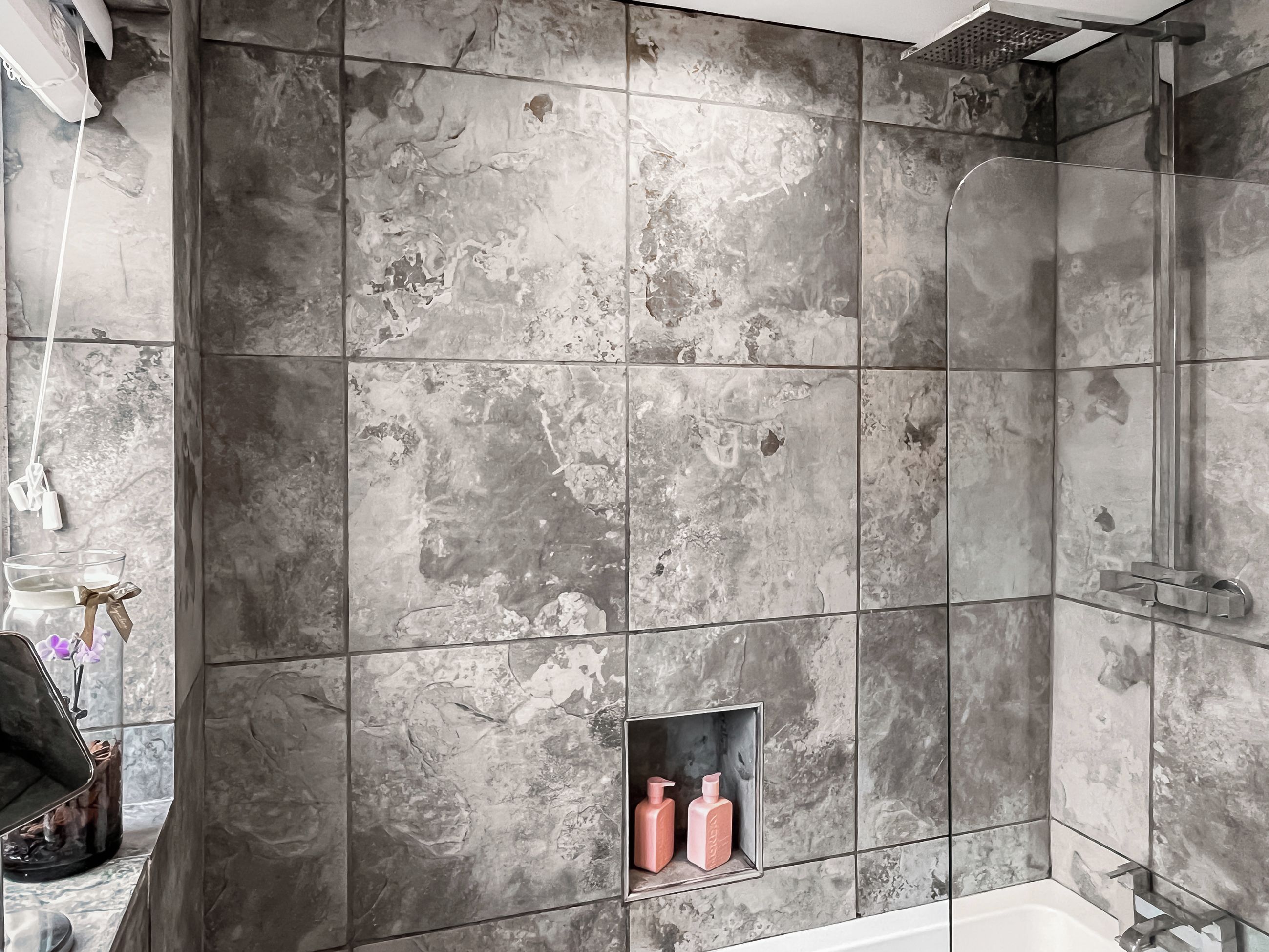 A bathroom with a shower, a built-in shelf with toiletries, and a mirror.