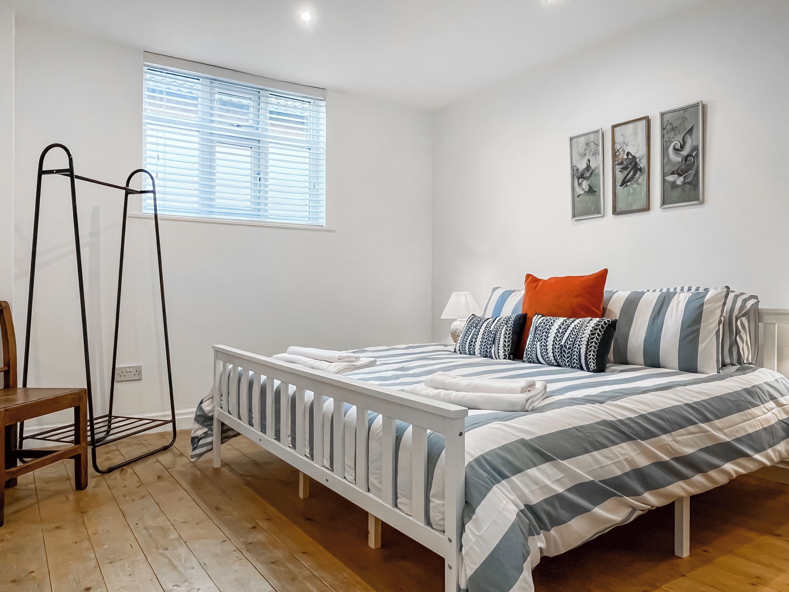 A bedroom with a bed, a window with blinds, a bedside table, and a chair.