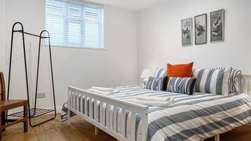 A bedroom with a bed, a window with blinds, a bedside table, and a chair.
