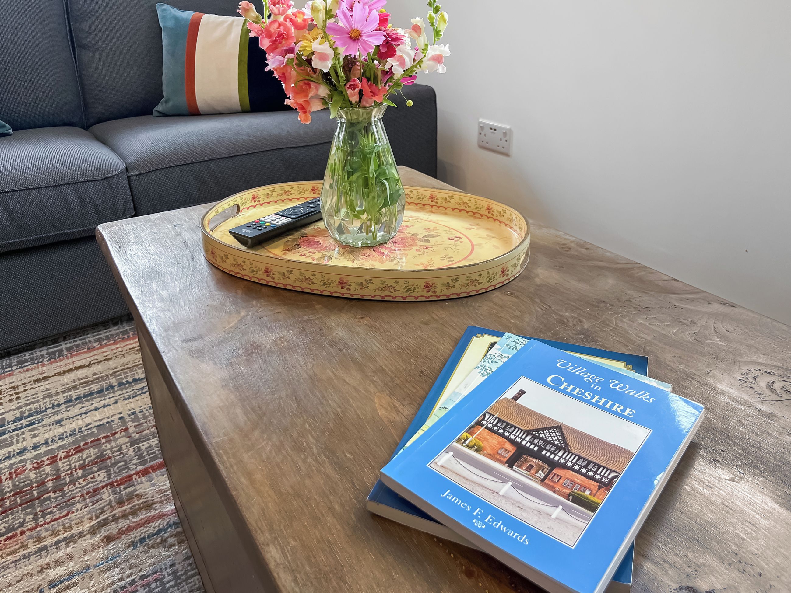 A living room with a sofa, a coffee table with a remote control, a vase with flowers, and a book titled 'Villa Chase'.