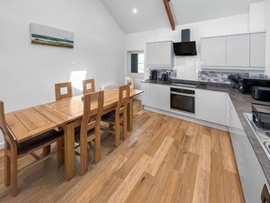 A modern kitchen with white cabinetry, a wooden dining table, and a herringbone-patterned floor.