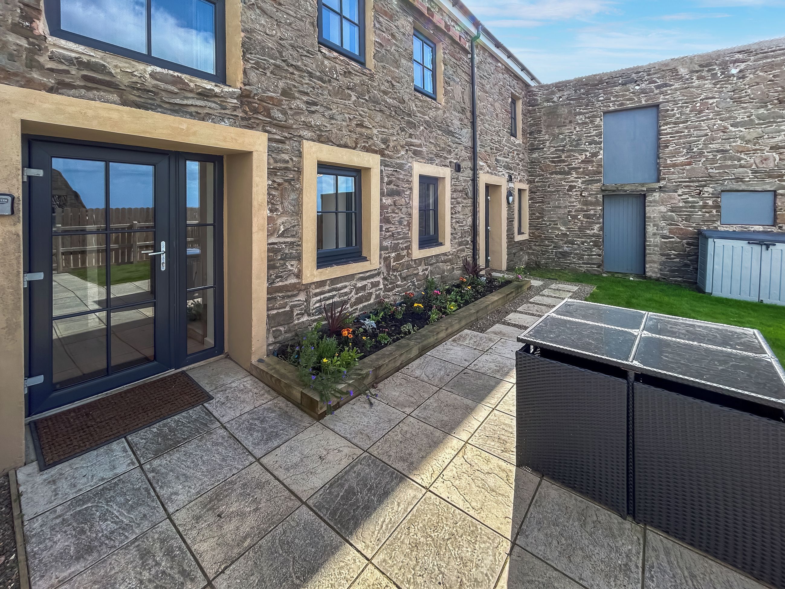 A stone building with a patio area, outdoor seating, and a small garden.