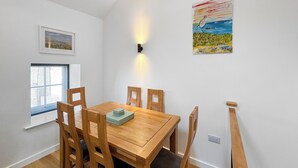 Een eethoek met een houten tafel en stoelen, een raam met zonwering en een wandlamp.