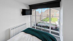 Een slaapkamer met een bed, een raam en uitzicht op een tuin.