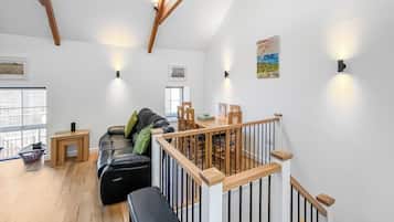 Amplia sala de estar con un sofá de cuero negro, mesa de comedor de madera y una escalera con barandilla de madera.