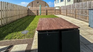 Een achtertuin met een houten terras, een groen gazon, een bakstenen muur en een houten omheining.
