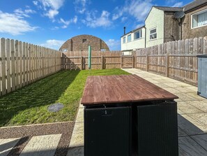 Un jardin avec une terrasse en bois, une pelouse verdoyante, un mur en briques et une clôture en bois.