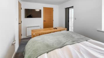 Un dormitorio con una cama, un banco de madera, un radiador, una puerta y una ventana.