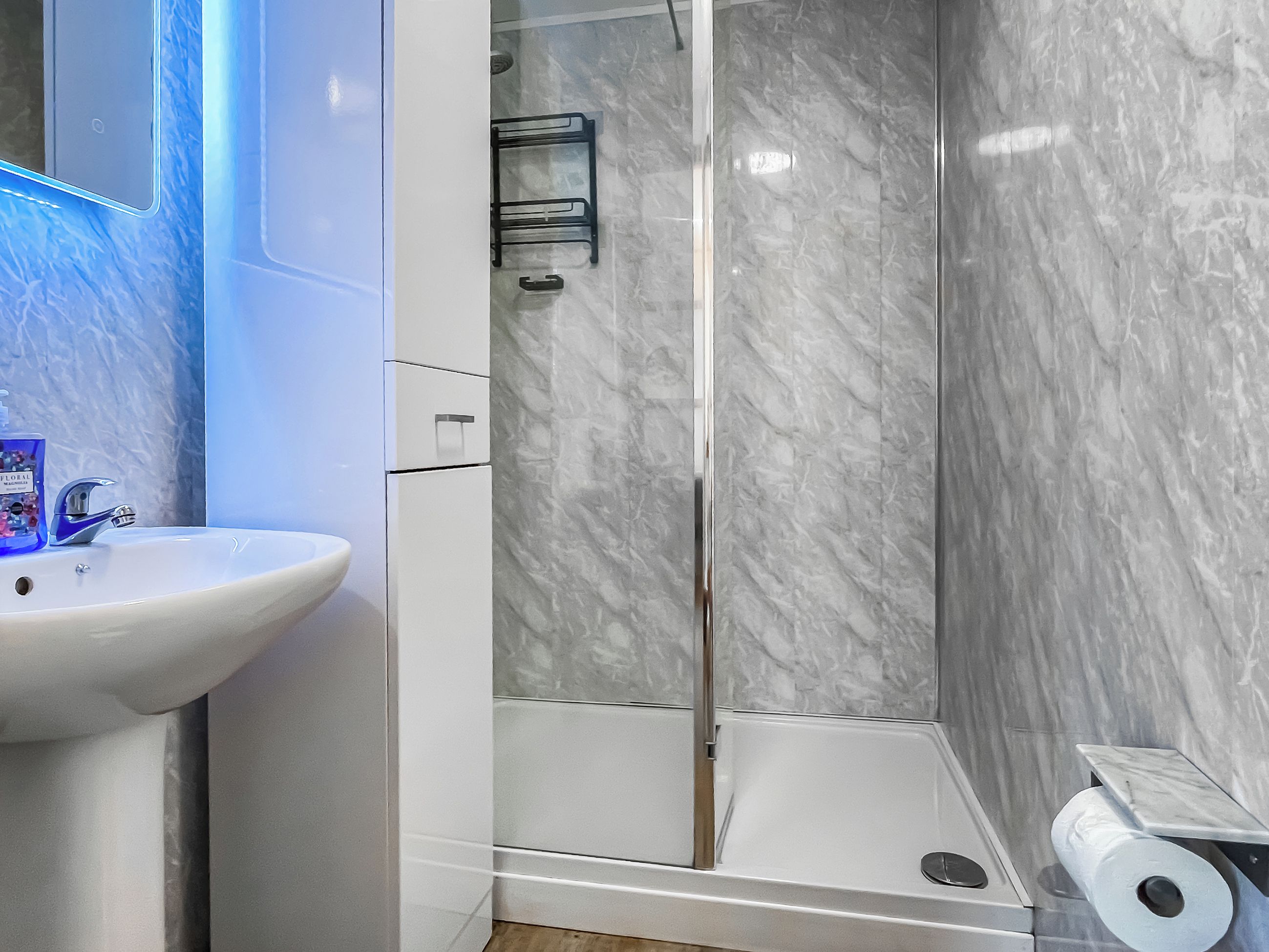 A bathroom with a white sink, a glass shower enclosure, and a marble wall.