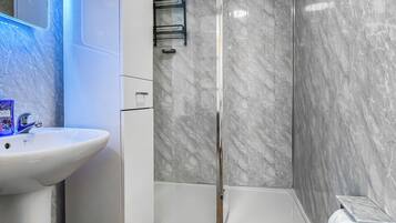 A bathroom with a white sink, a glass shower enclosure, and a marble wall.