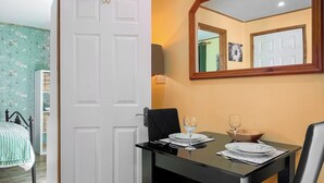Un comedor con una mesa dispuesta para dos, una puerta blanca, un espejo y una estantería con papel tapiz floral.