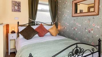 Ein Bett mit Kopfteil, ein Nachttisch mit Lampe und blumigem Wandpapier.