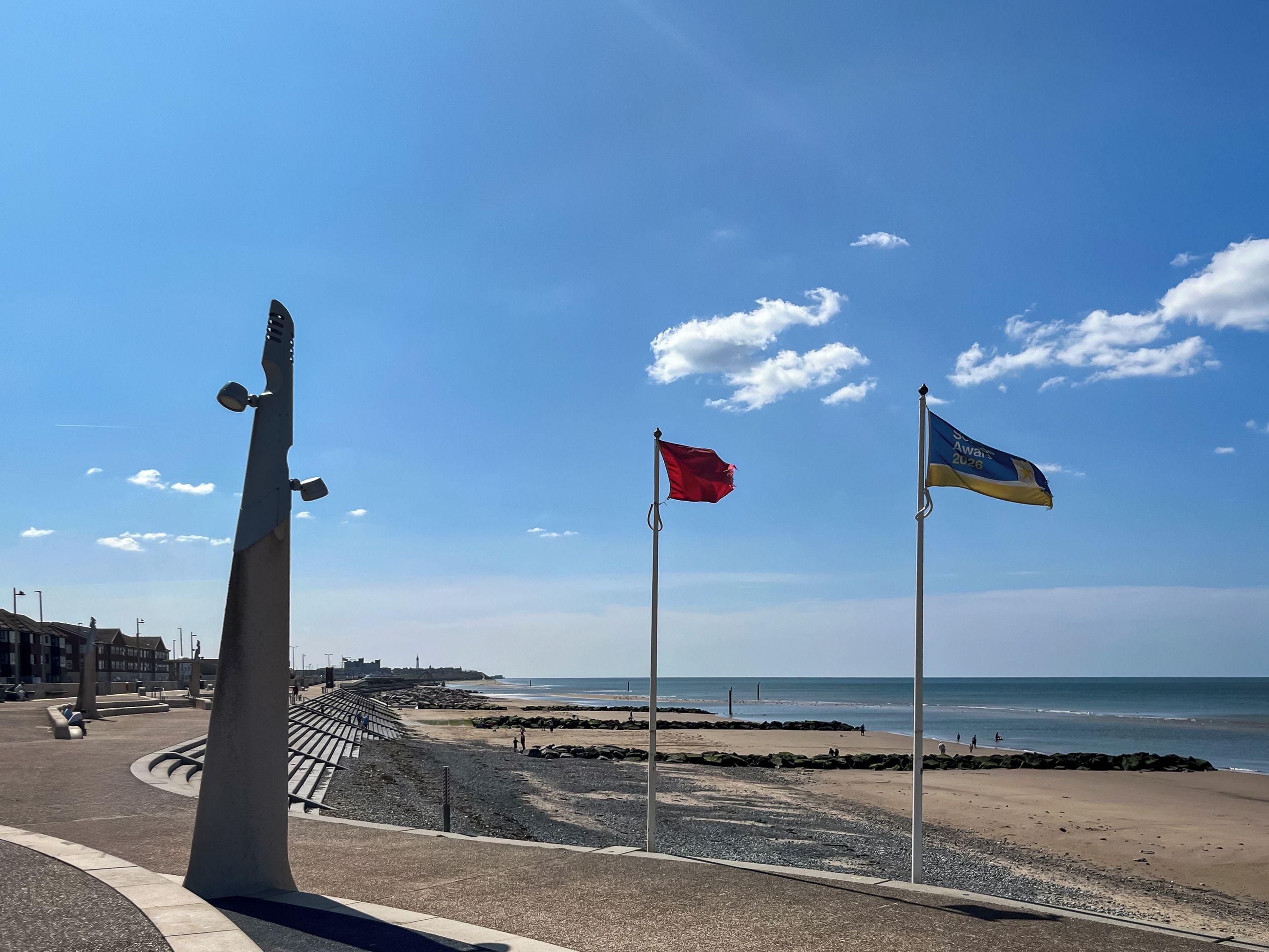 Una playa con un asta de bandera, una escultura y cielo despejado.