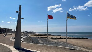 Una playa con un asta de bandera, una escultura y cielo despejado.