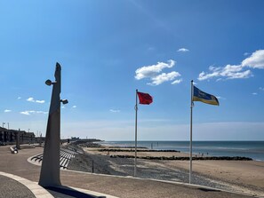 Una platja amb un penya-segat, una escultura i un cel serè.